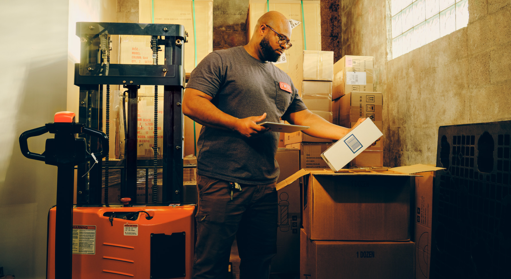 A person in a warehouse holds a box with their left hand and an iPad with their right hand while taking inventory on the device. A diagram to the right of the image shows the features of the [content00inject]5[content00inject] Inventory platform.